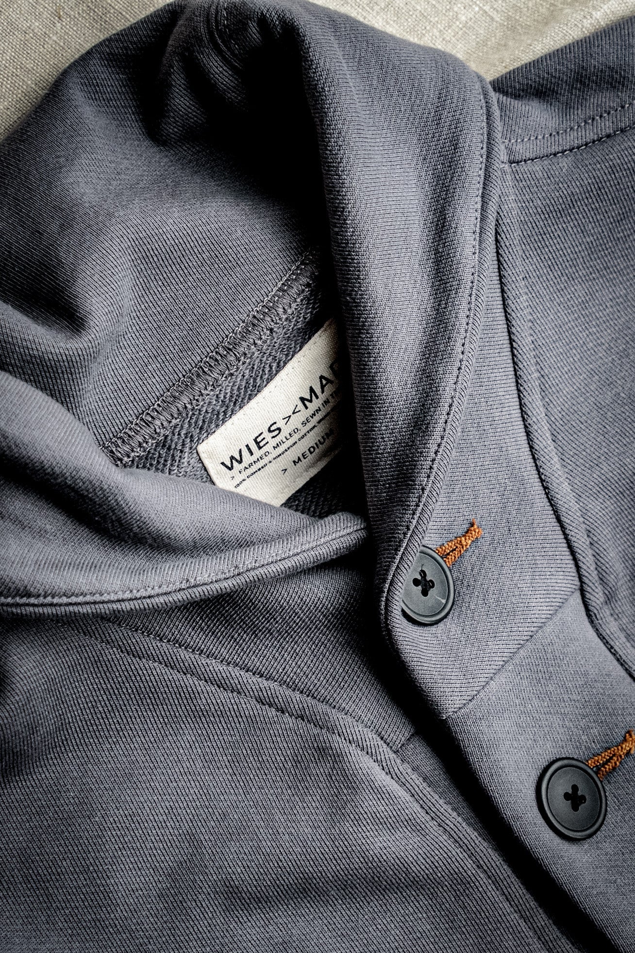 Close-up of pebble grey French terry shawl cardigan showing WiesMade label, dark buttons, and tobacco contrast keyholes.