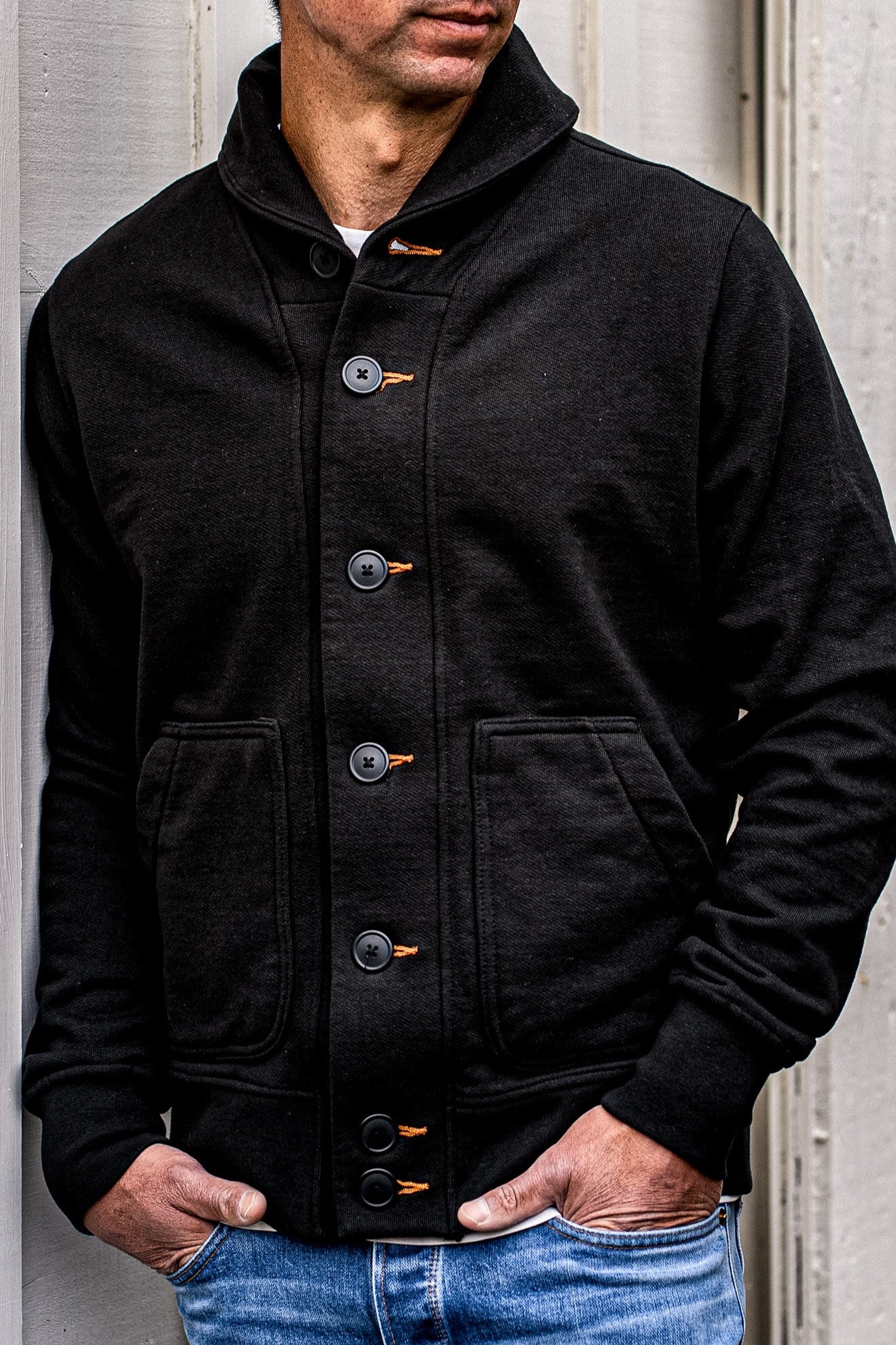 Man wearing black shawl collar Bodega cardigan with contrast tobacco keyhole stitching and denim jeans.