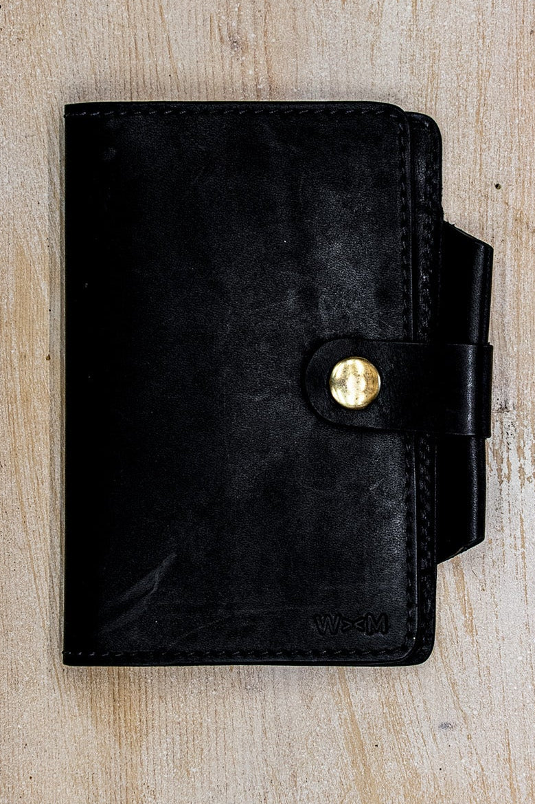Black Horween leather Field Notes cover with brass snap closure on weathered wood.
