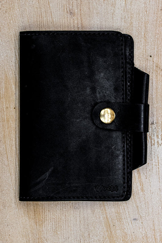 Black Horween leather Field Notes cover with brass snap closure on weathered wood.