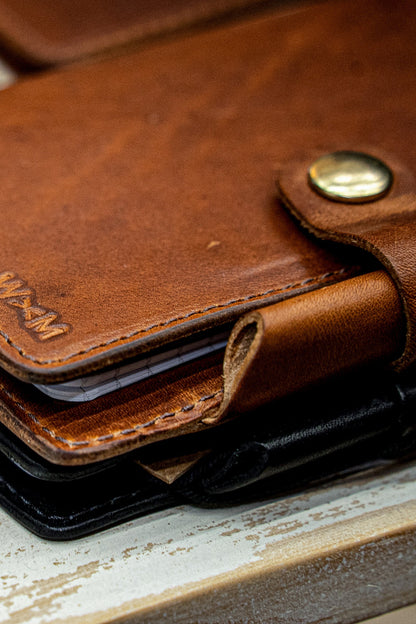 Tan Horween leather Field Notes cover with brass snap and embossed WM logo, stacked on black.