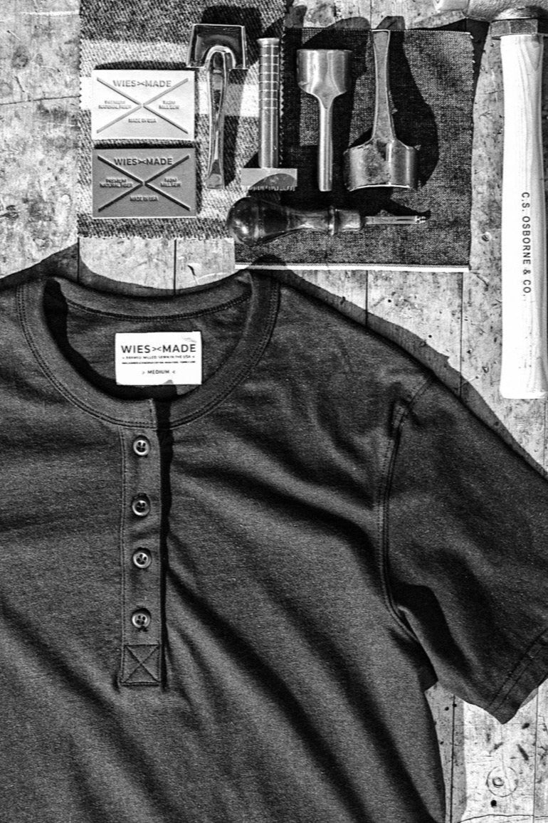 Navy four-button Reyes Henley laid flat on a workbench with leatherworking tools and WiesMade labels.