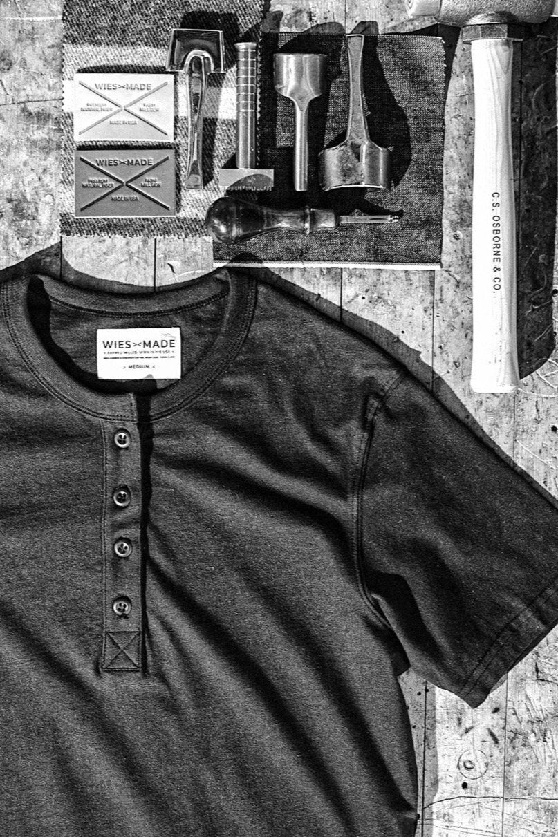 Olive four-button Reyes Henley shirt laid flat on a workbench with leather tools and WiesMade labels.