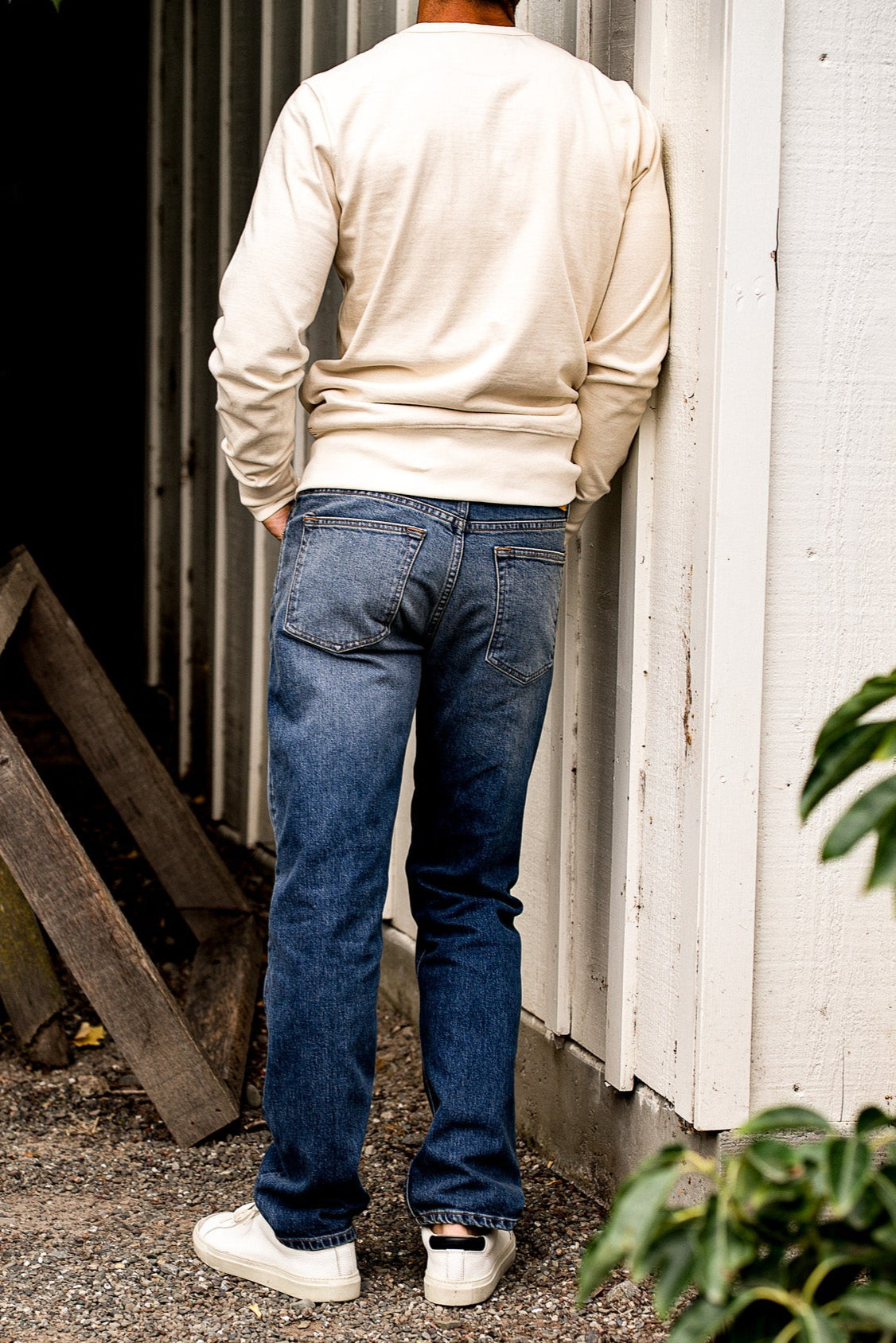 Man near a white wall wearing a beige sweater and premium denim jeans