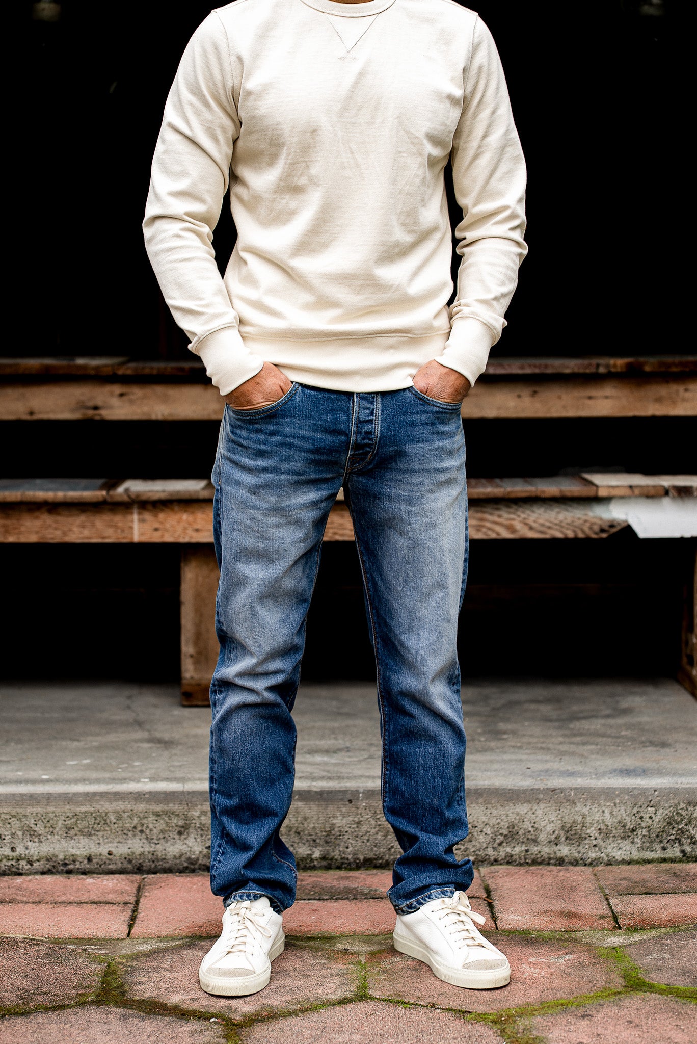 Close-up of a man wearing loose straight cut denim jeans and a beige sweater on a paved patio