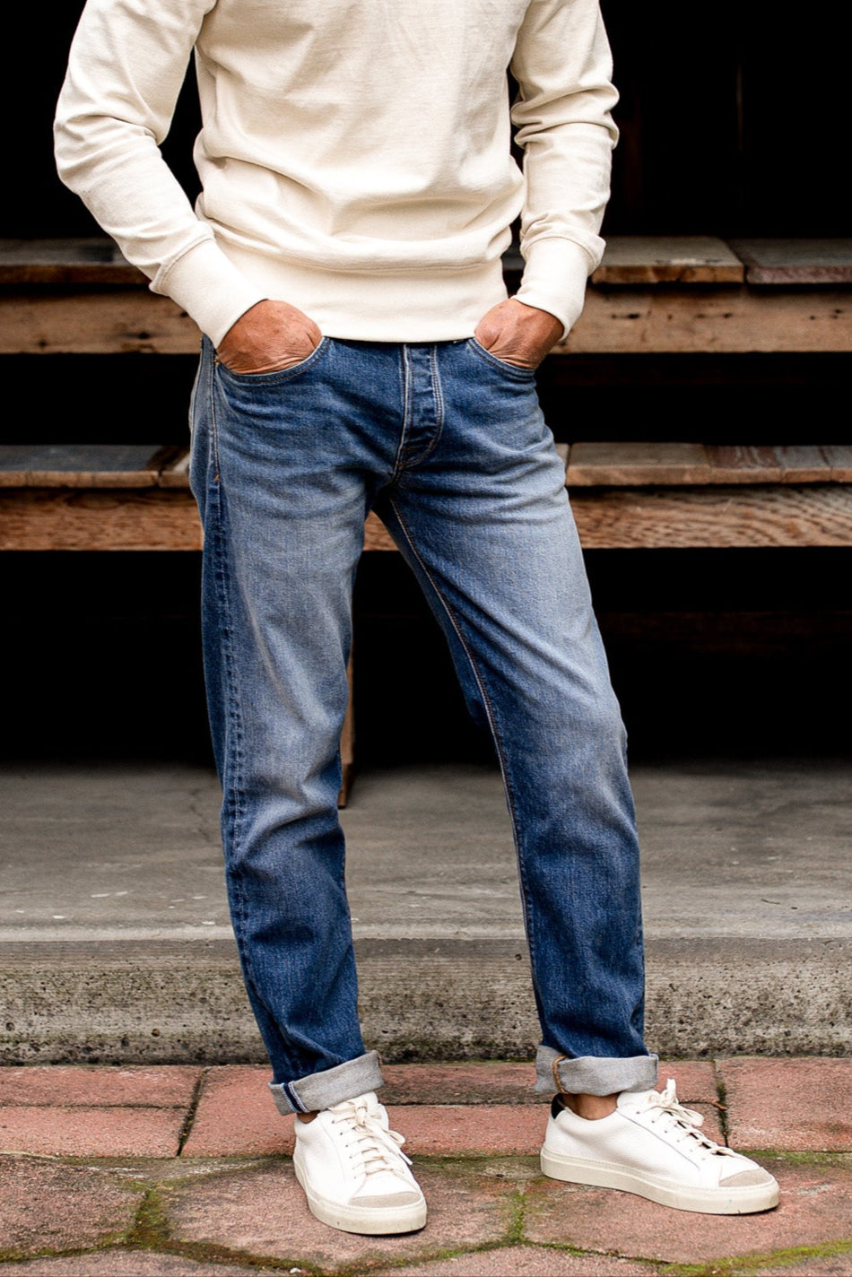Man modeling loose straight fit jeans made in USA, paired with a white sweater and sneakers