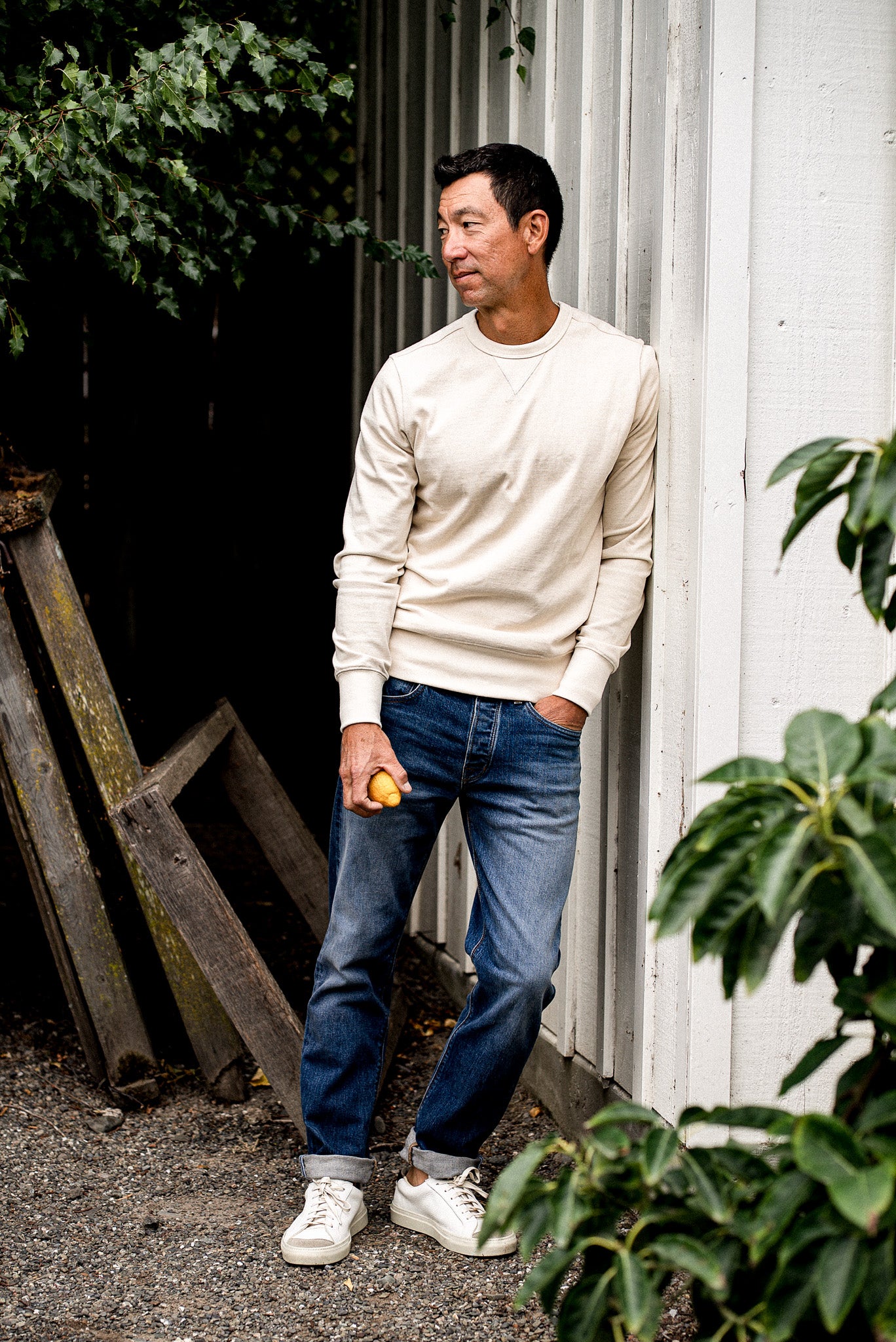 Man outdoors near plants wearing a white sweater and men's denim jeans made in USA