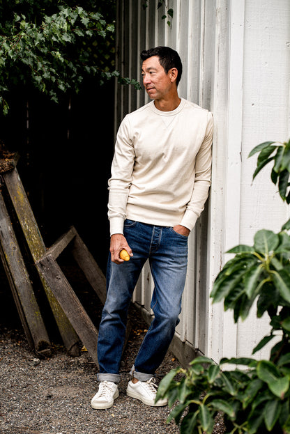 Man outdoors near plants wearing a white sweater and men's denim jeans made in USA