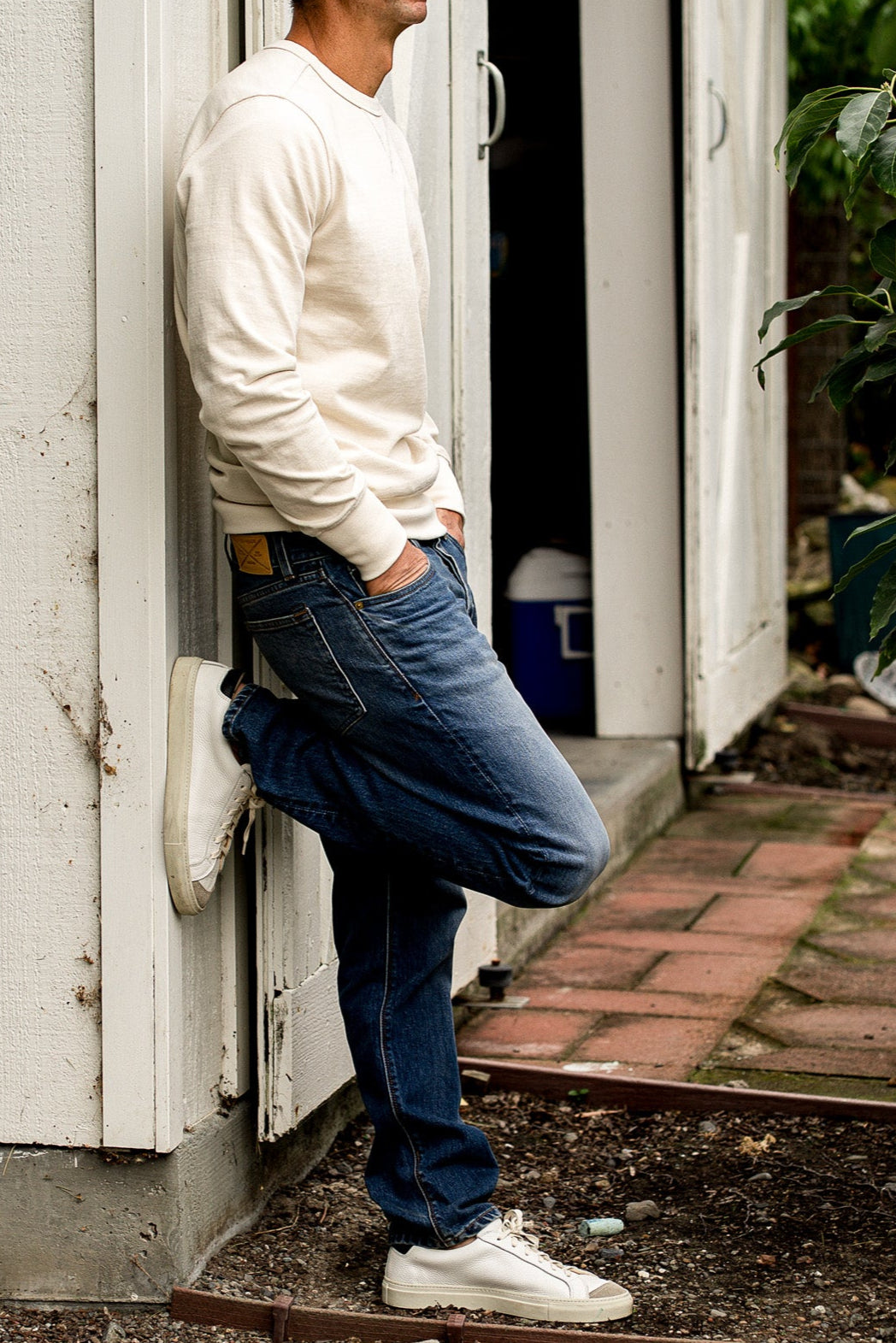 Man leaning against a white door wearing denim jeans made in USA with a white shirt