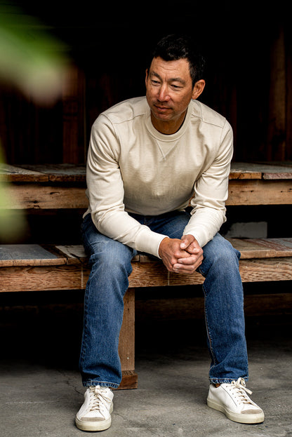 Man sitting on a wooden bench wearing premium denim jeans and a white sweater
