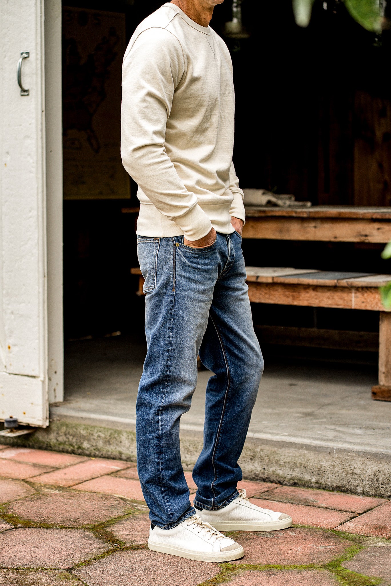 Man standing on a patio wearing a beige sweater and loose straight fit jeans made in USA