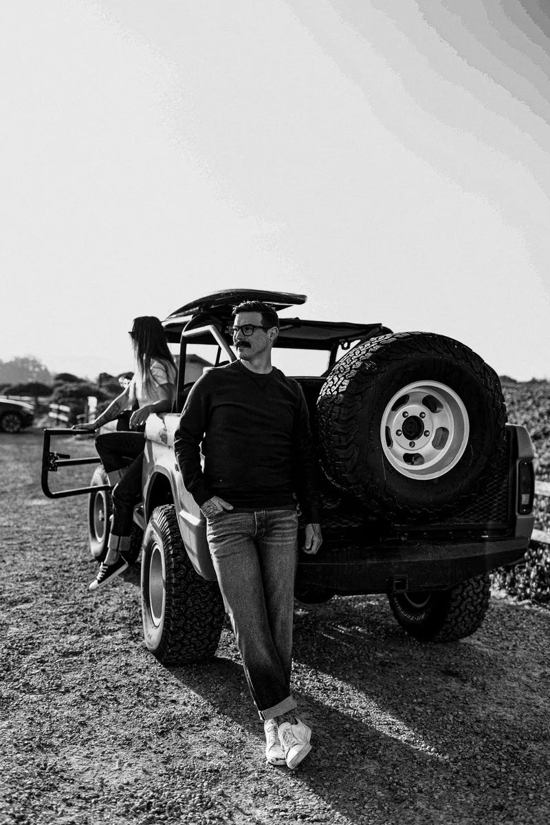 Man wearing American-made salt wash jeans, leaning against a vintage off-road truck.