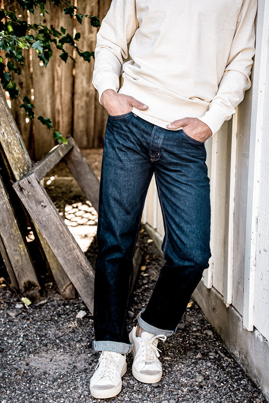 Man in cream sweatshirt and cuffed ocean wash loose straight American made denim jeans with white sneakers.