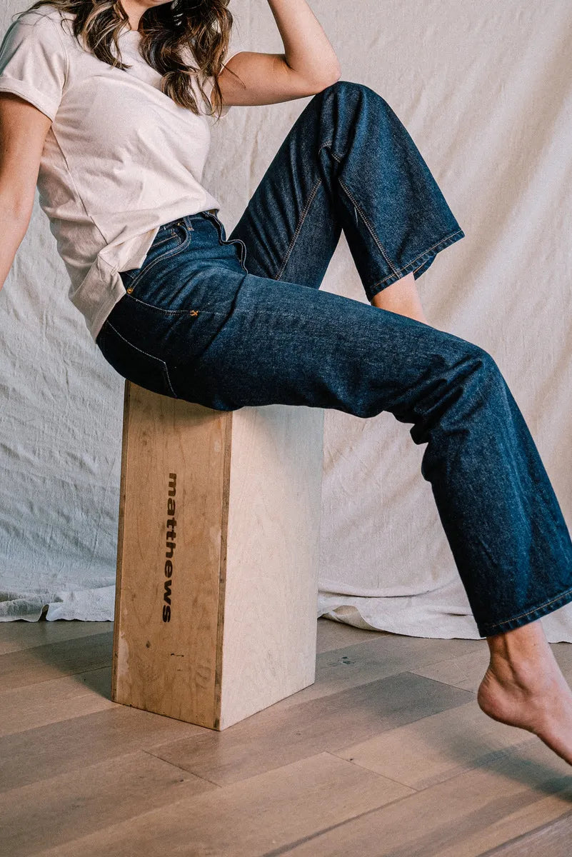 Person seated on a wooden box wearing ocean wash mid-rise wide-leg jeans with white tee.