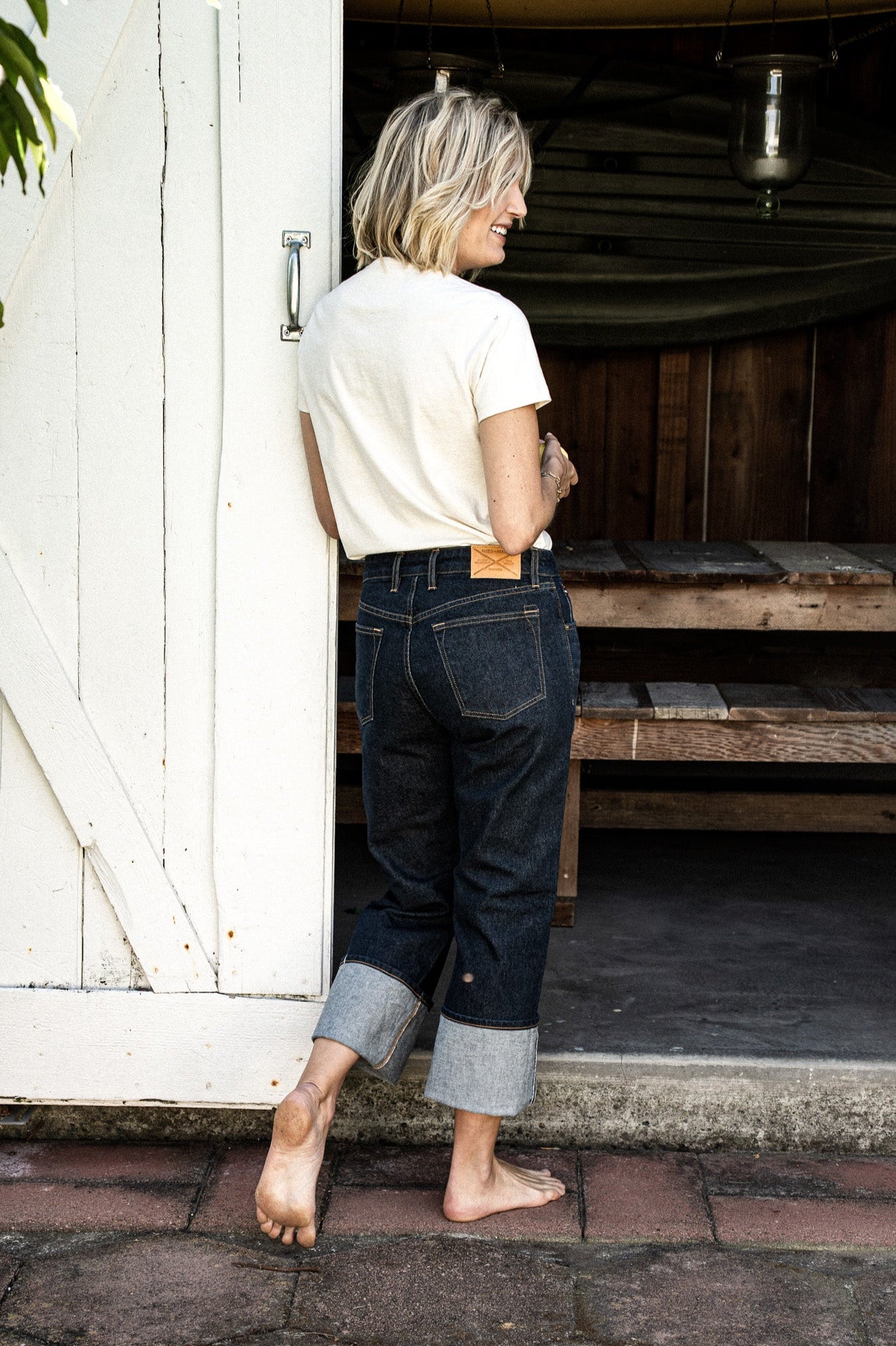 Back view of cuffed Jackie wide-leg jeans in ocean wash denim, worn with a cream tee in a doorway.