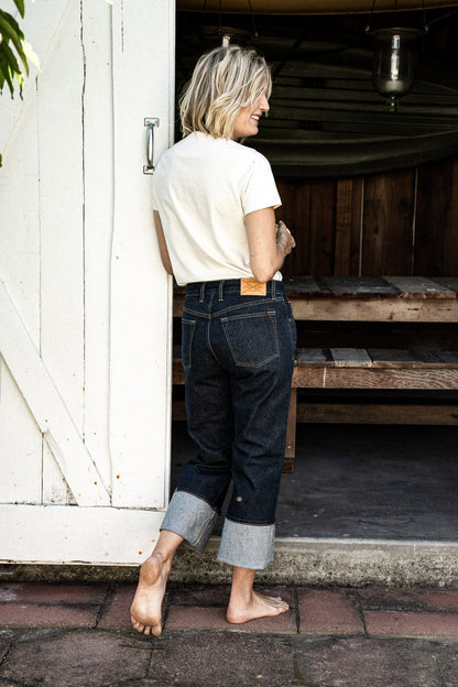 Back view of cuffed Jackie wide-leg jeans in ocean wash denim, worn with a cream tee in a doorway.