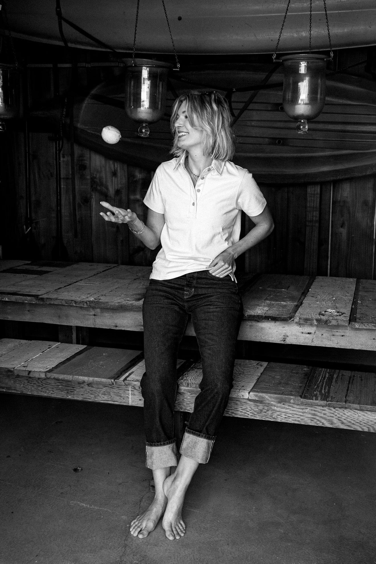 Woman in cuffed wide-leg American made jeans and a white polo, leaning on a wooden bench.