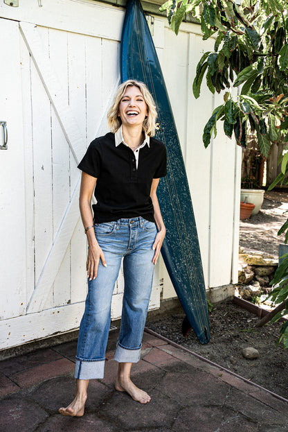 Designer mid-rise denim jeans for women styled with a black collared shirt, featuring a relaxed fit, light wash finish, and cuffed hems that create an easy, coastal-inspired look