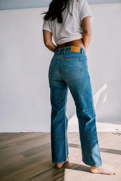 Woman wearing Jackie Fit Jean in Salt Wash color with a mid-rise wide leg, standing barefoot on a wooden floor against a neutral backdrop