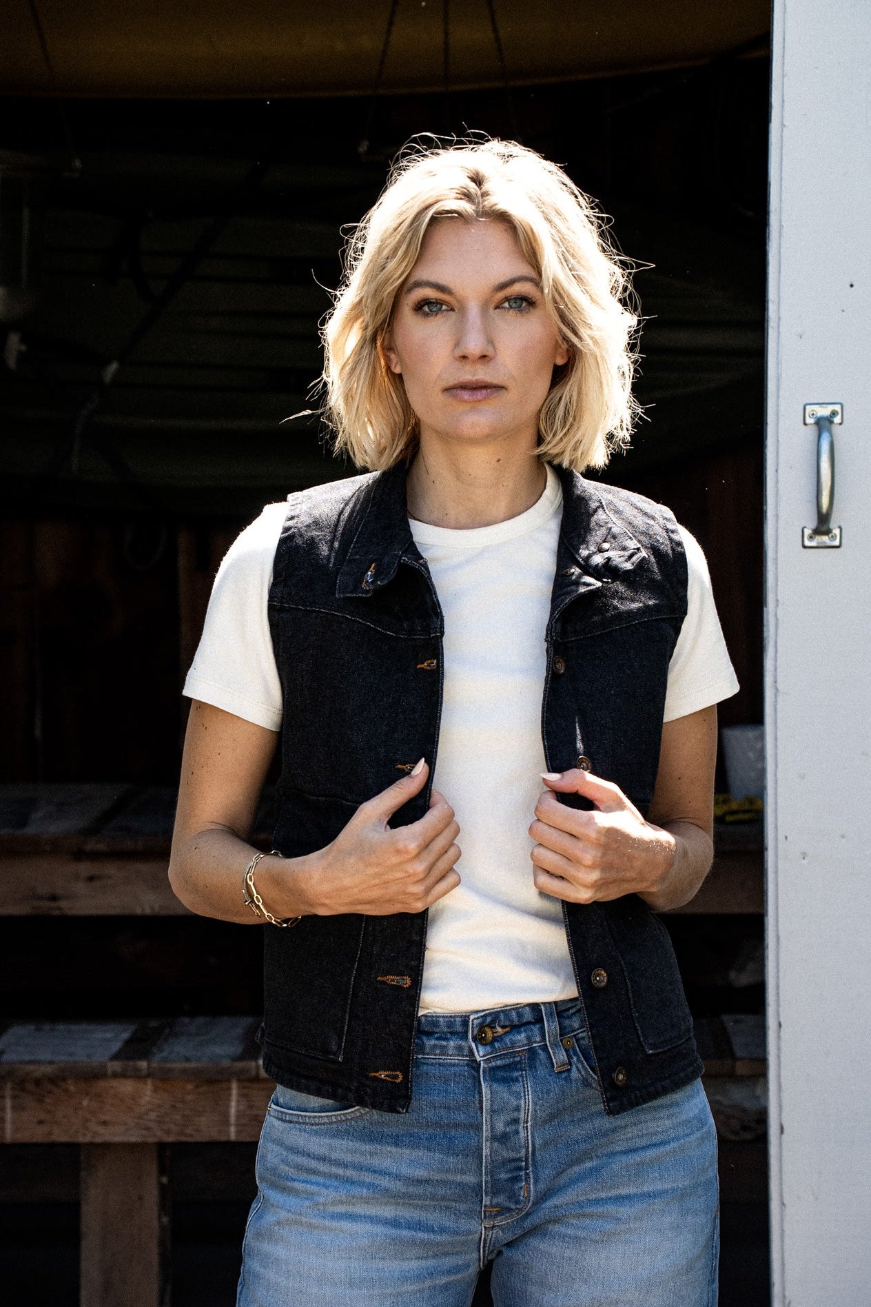 Woman wearing black broken twill denim vest over white tee with blue jeans.
