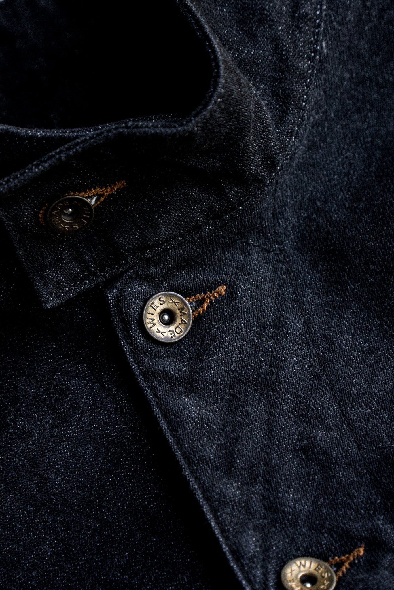 Close-up of black broken twill denim vest with brass WiesMade buttons and tobacco keyhole stitching.