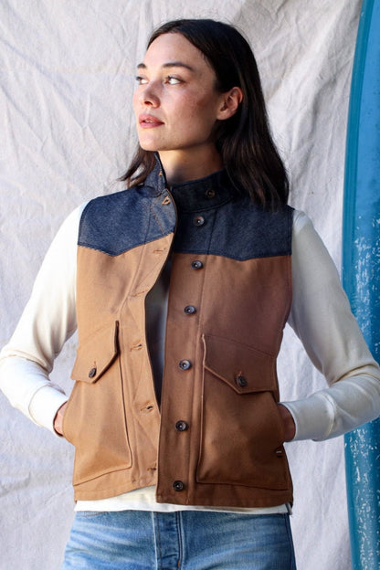Woman wearing a tan canvas Jamie vest with denim yoke, button front, and flap pockets over a cream long-sleeve top.