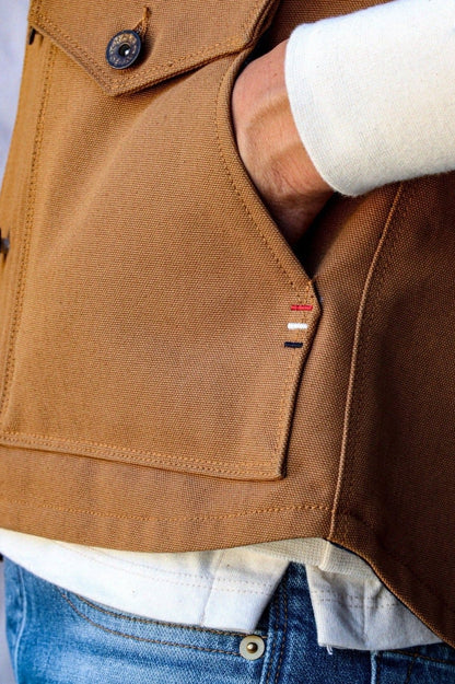 Close-up of tan canvas Jamie Vest showing hand tucked into wool-lined pocket over cream sweater and jeans.