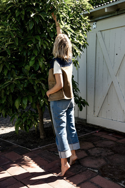 Back view of the wheat Jamie denim vest worn outdoors reaching into a leafy tree.
