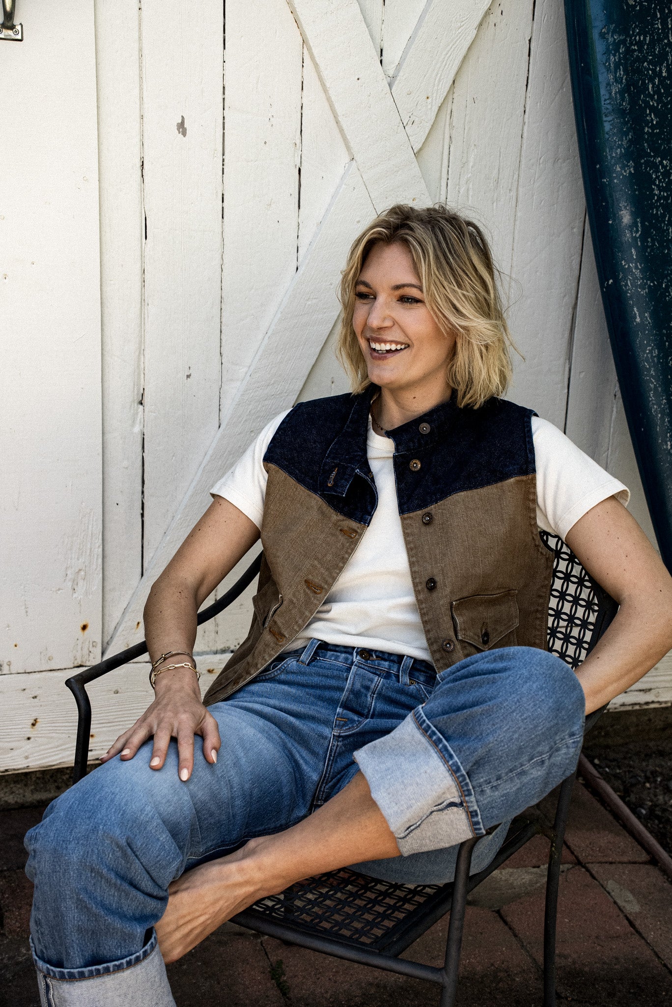 Seated woman wearing the wheat broken twill denim vest over a white tee and blue jeans.