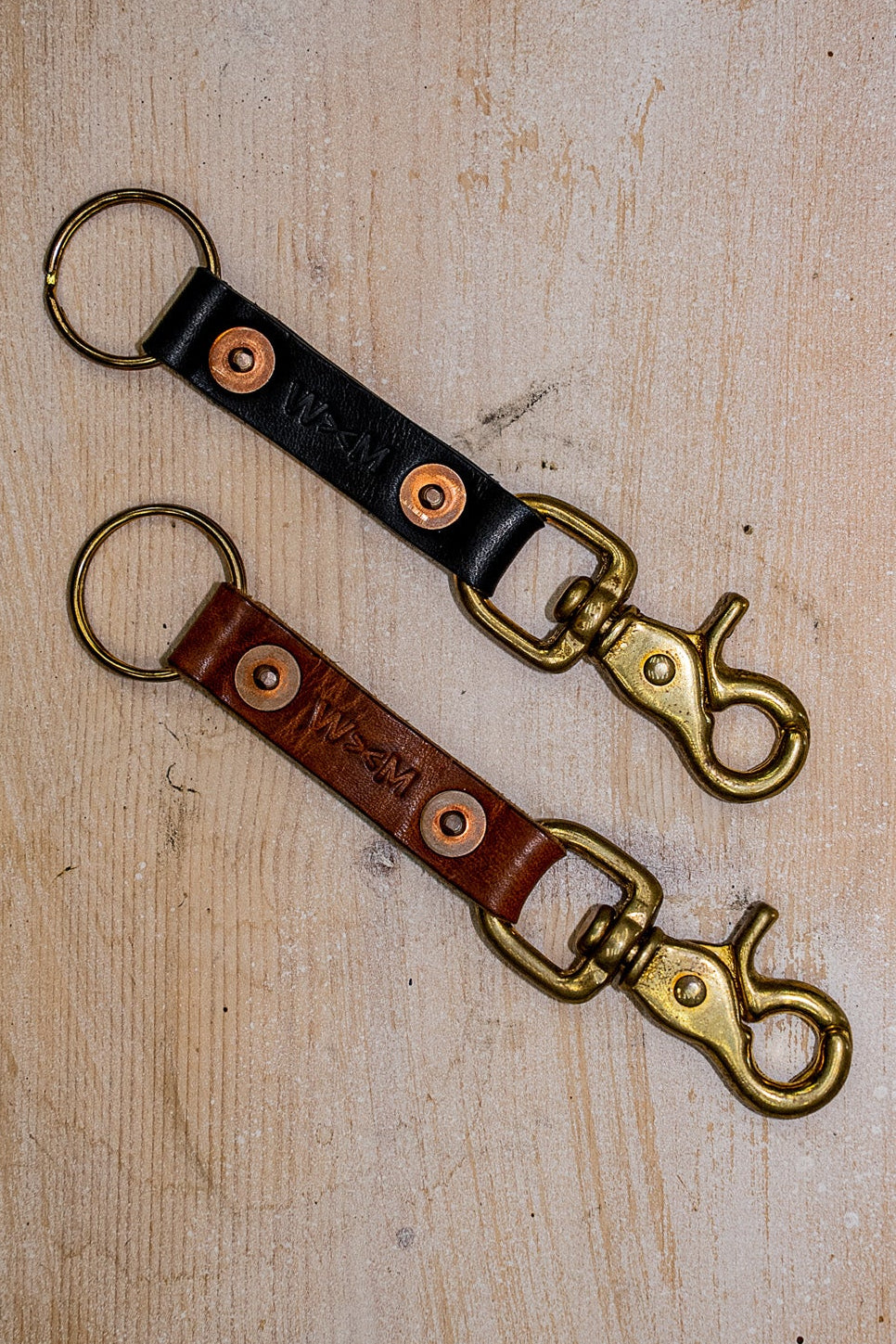 Tan and black Horween leather key clips with brass swivel clasps and copper rivets.