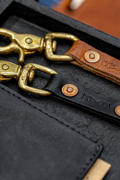 Tan and black Horween leather key clips with brass swivel clasps and copper rivets.