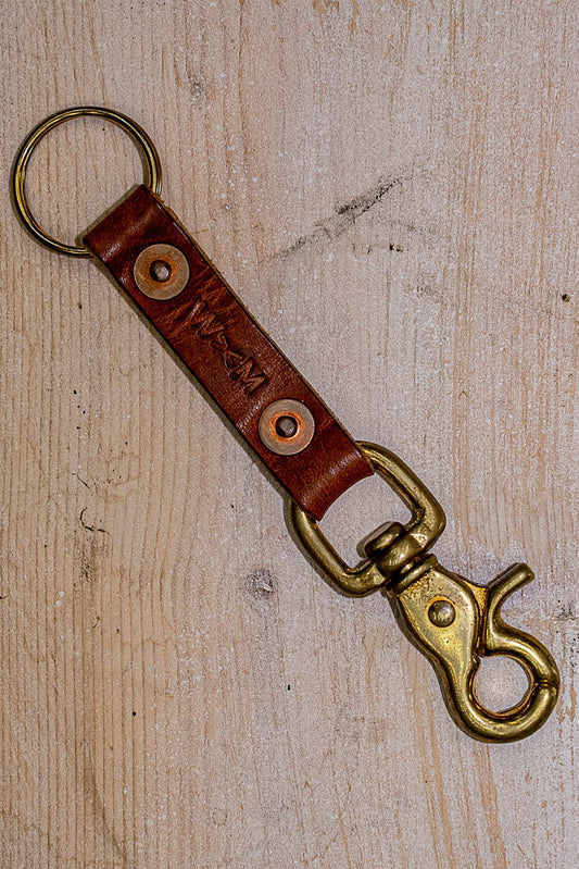 Tan Horween leather key clip with brass swivel clasp and split ring on wood.