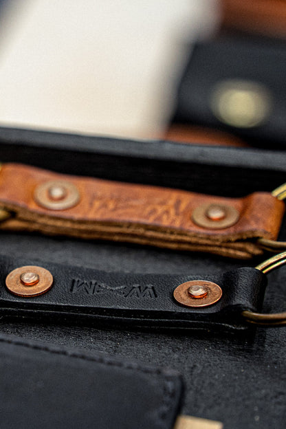 Tan and black Horween leather key clips with copper rivets and brass rings.