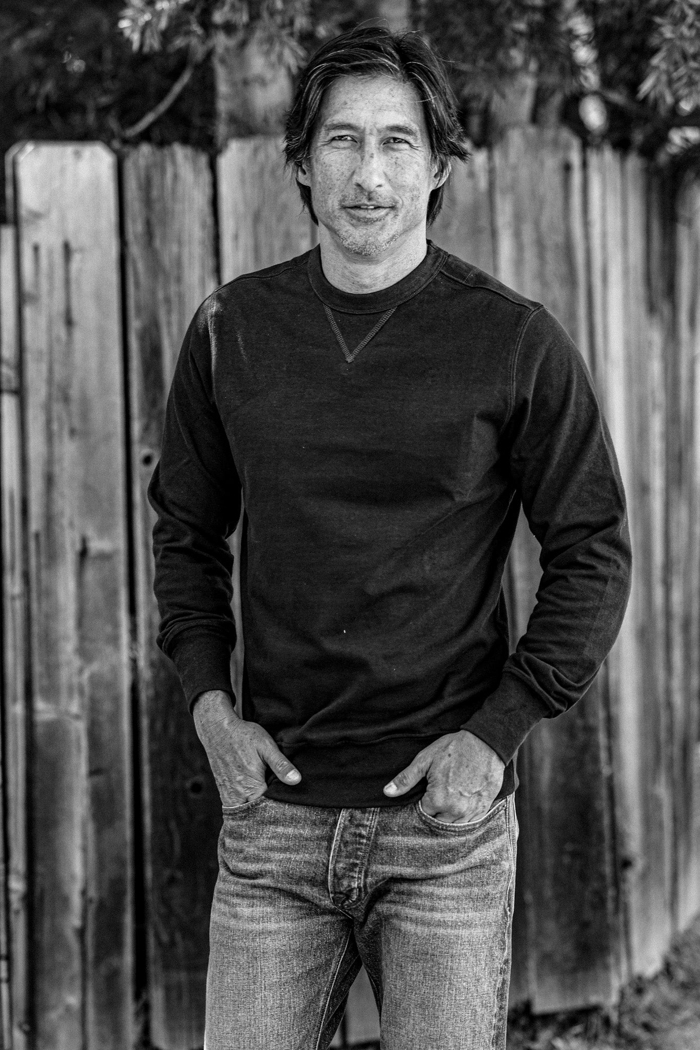 Man wearing the Stinson basalt rugby jersey pullover with jeans, standing by a wooden fence.