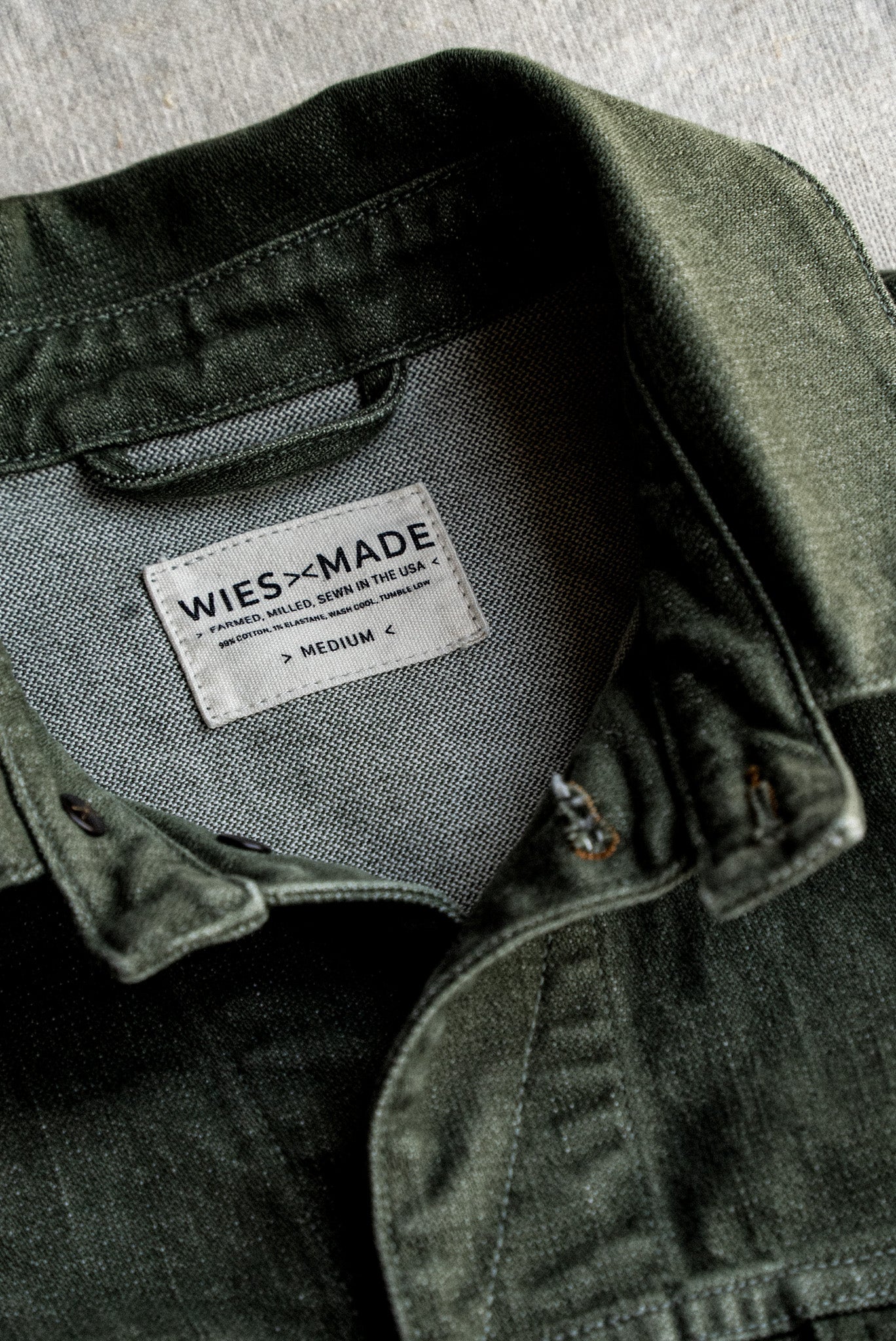 Close-up of olive broken twill denim jacket collar with WiesMade inner label noting farmed, milled, and sewn in the USA.
