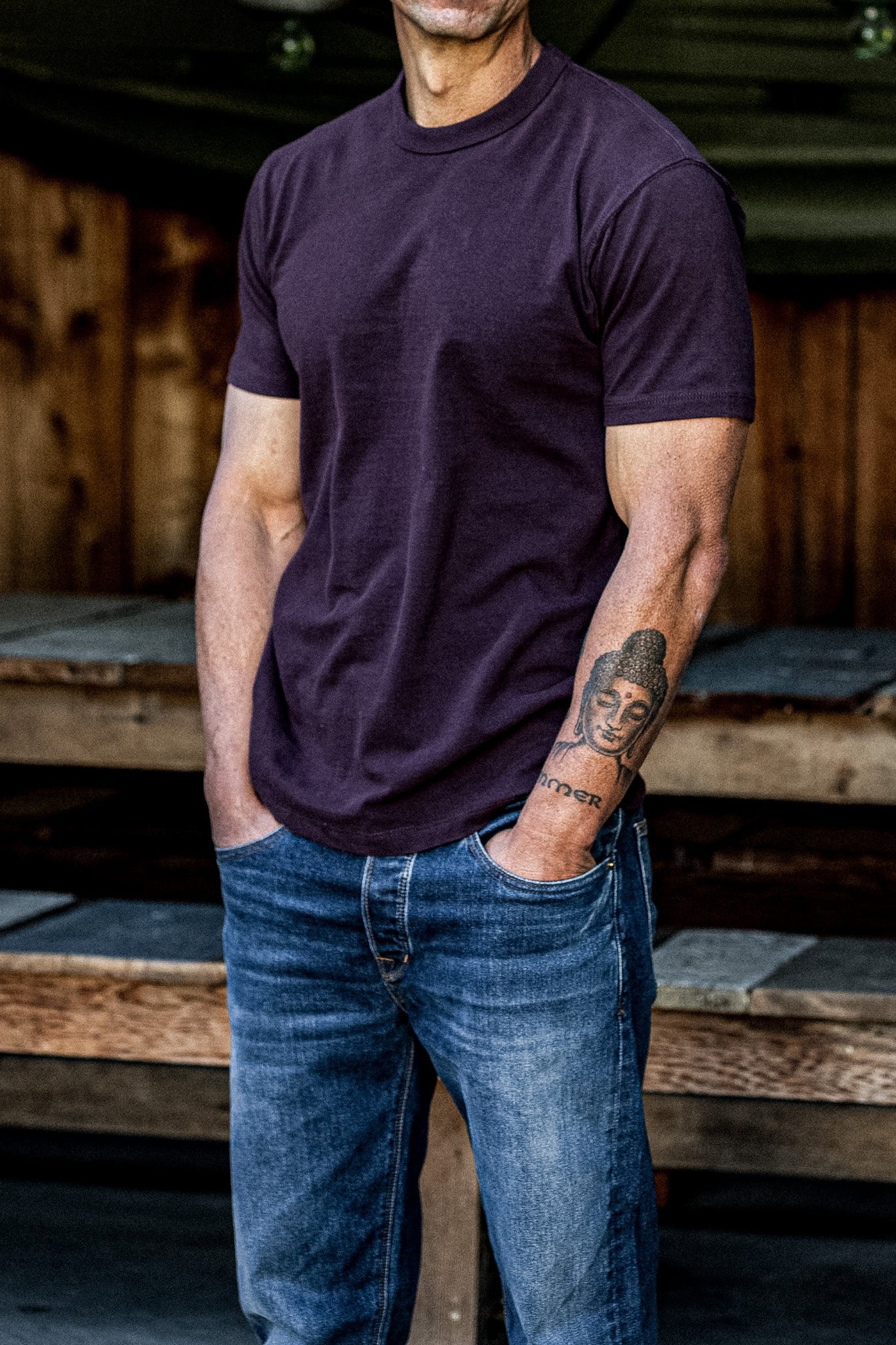 Man wearing oxblood heavyweight cotton Bolinas tee with blue jeans by a wooden barn.