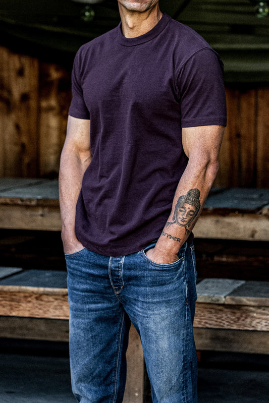 Man wearing oxblood heavyweight cotton Bolinas tee with blue jeans by a wooden barn.