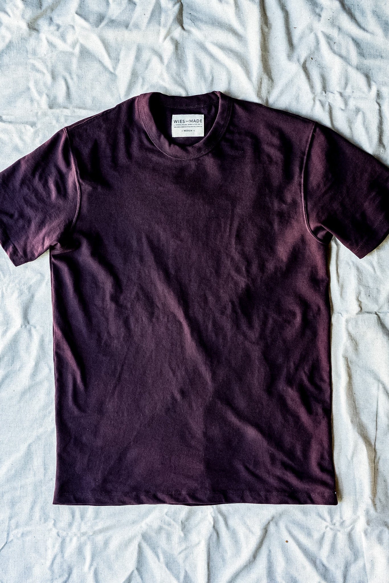 Oxblood heavyweight cotton Bolinas tee laid flat on a wrinkled natural linen backdrop.