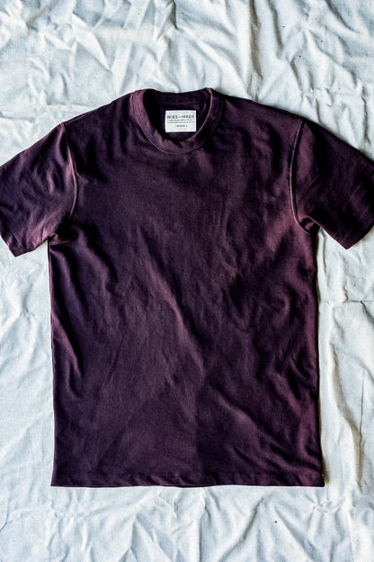Oxblood heavyweight cotton Bolinas tee laid flat on a wrinkled natural linen backdrop.