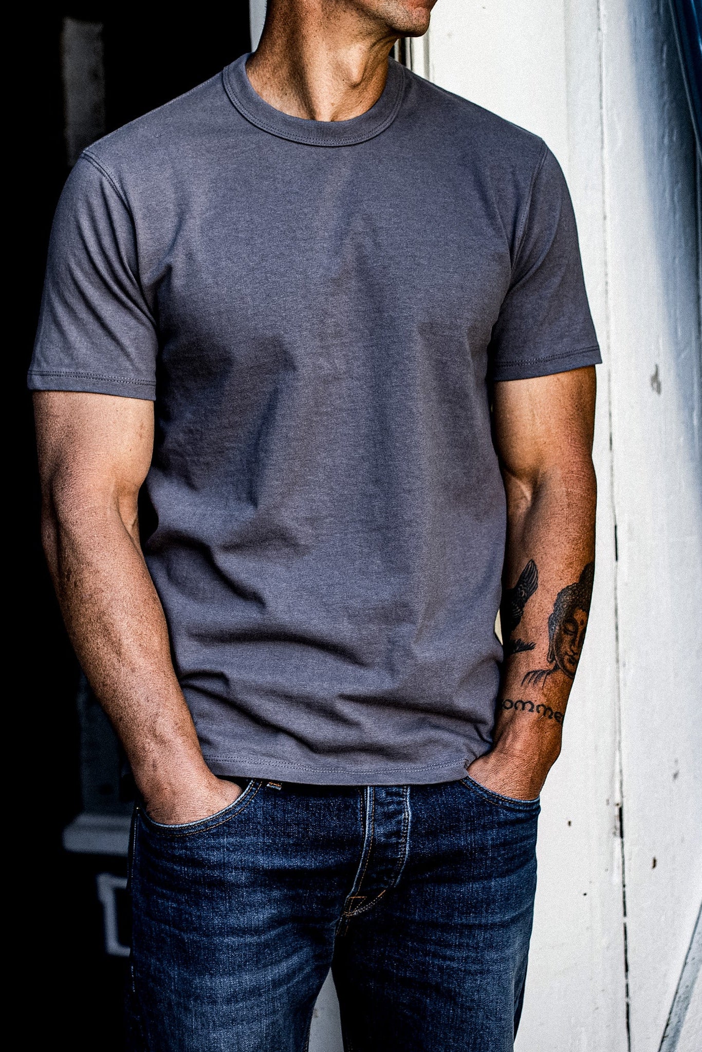 Man wearing pebble gray t-shirt and jeans standing against a white wall