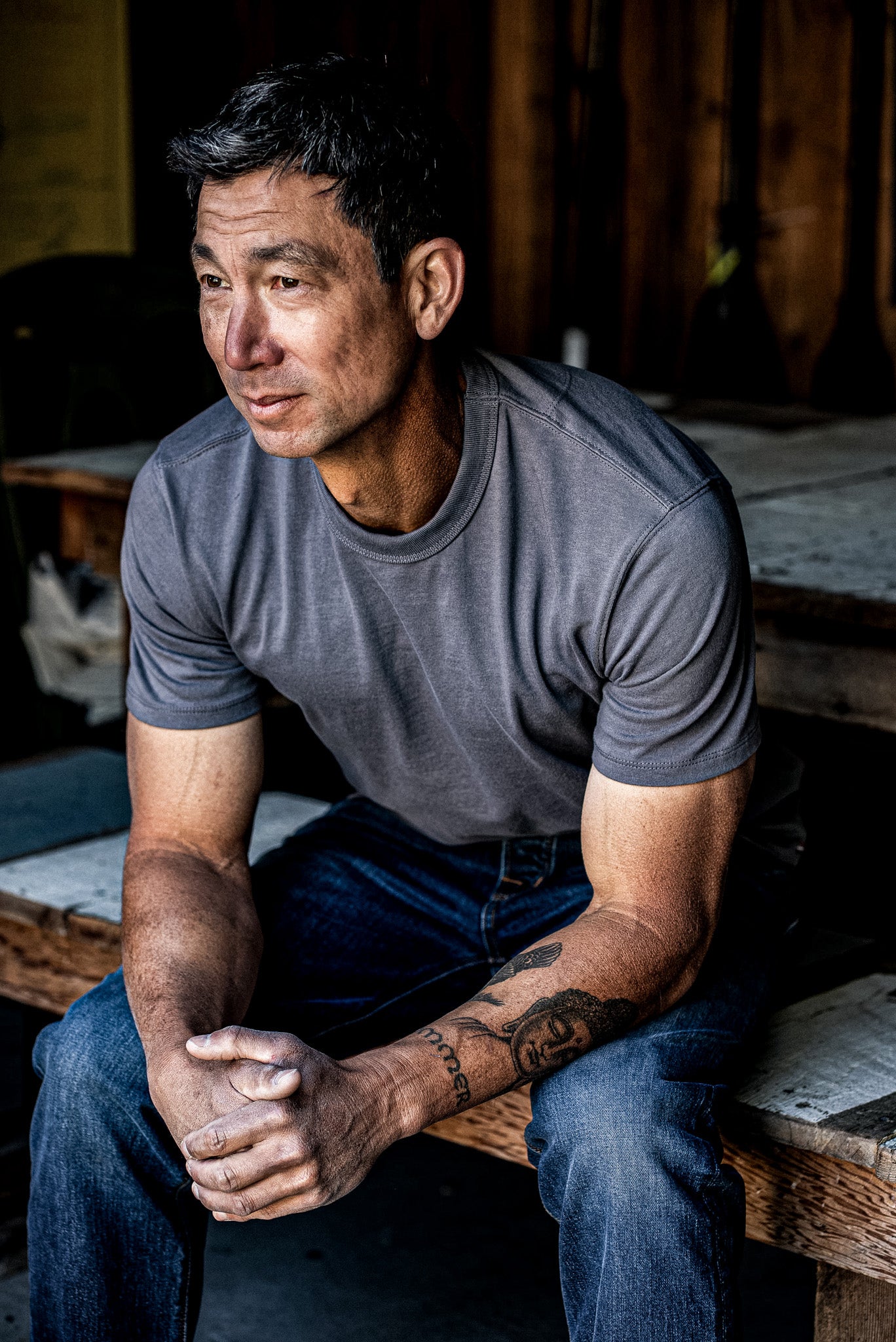 Man sitting outdoors wearing pebble gray t-shirt and blue jeans