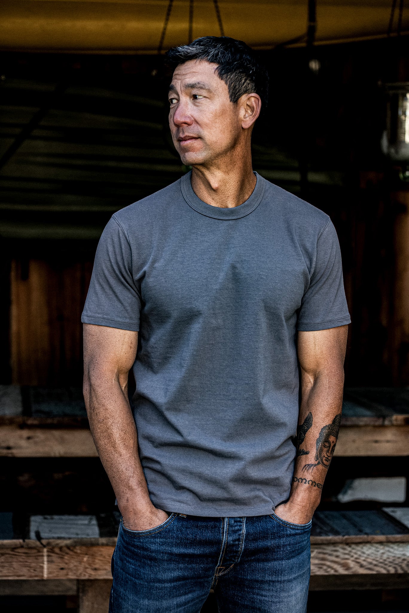 Man wearing pebble gray t-shirt and jeans in a rustic indoor setting