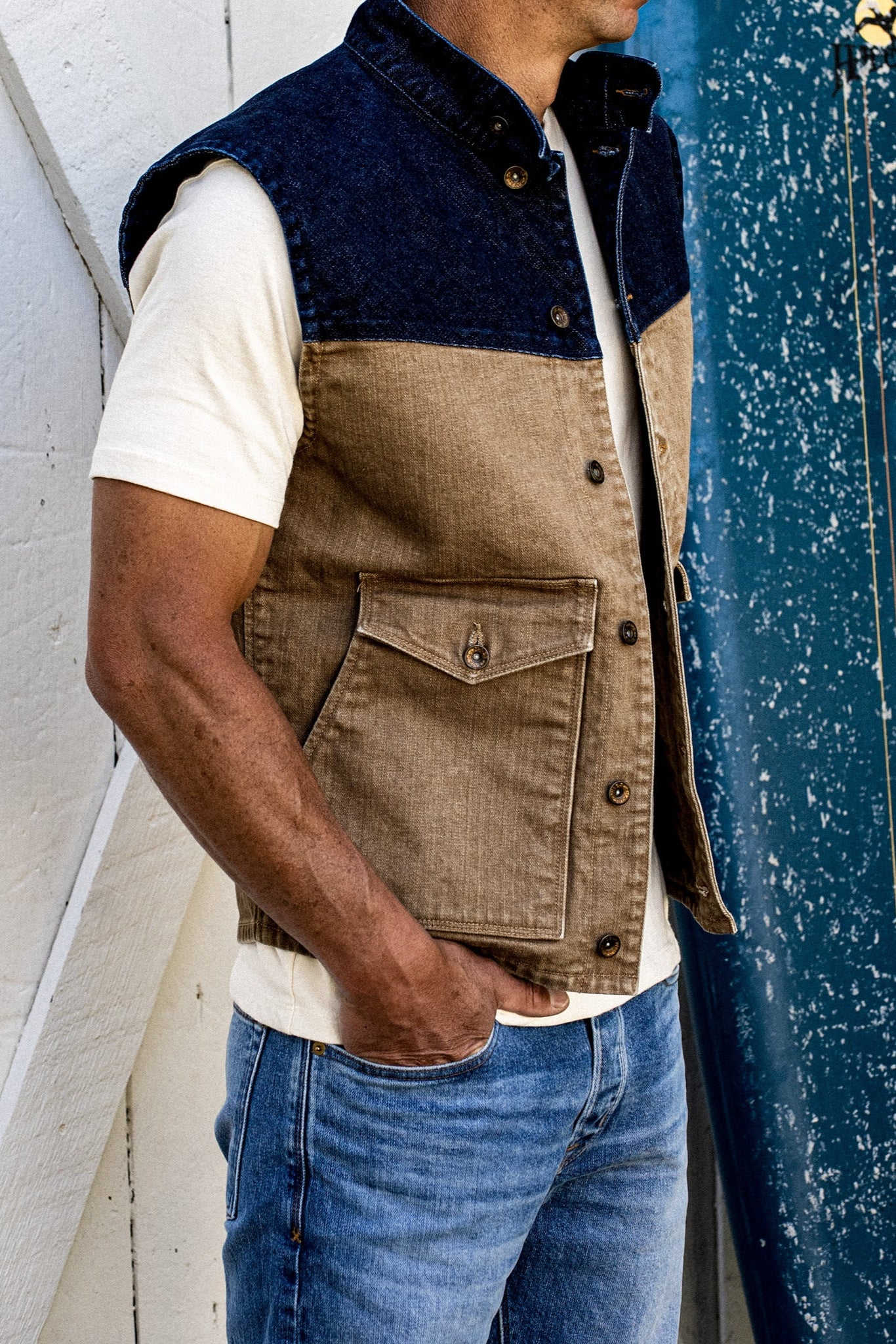 Side view of the James two-tone broken twill denim vest in wheat and indigo, worn over a cream tee with jeans.