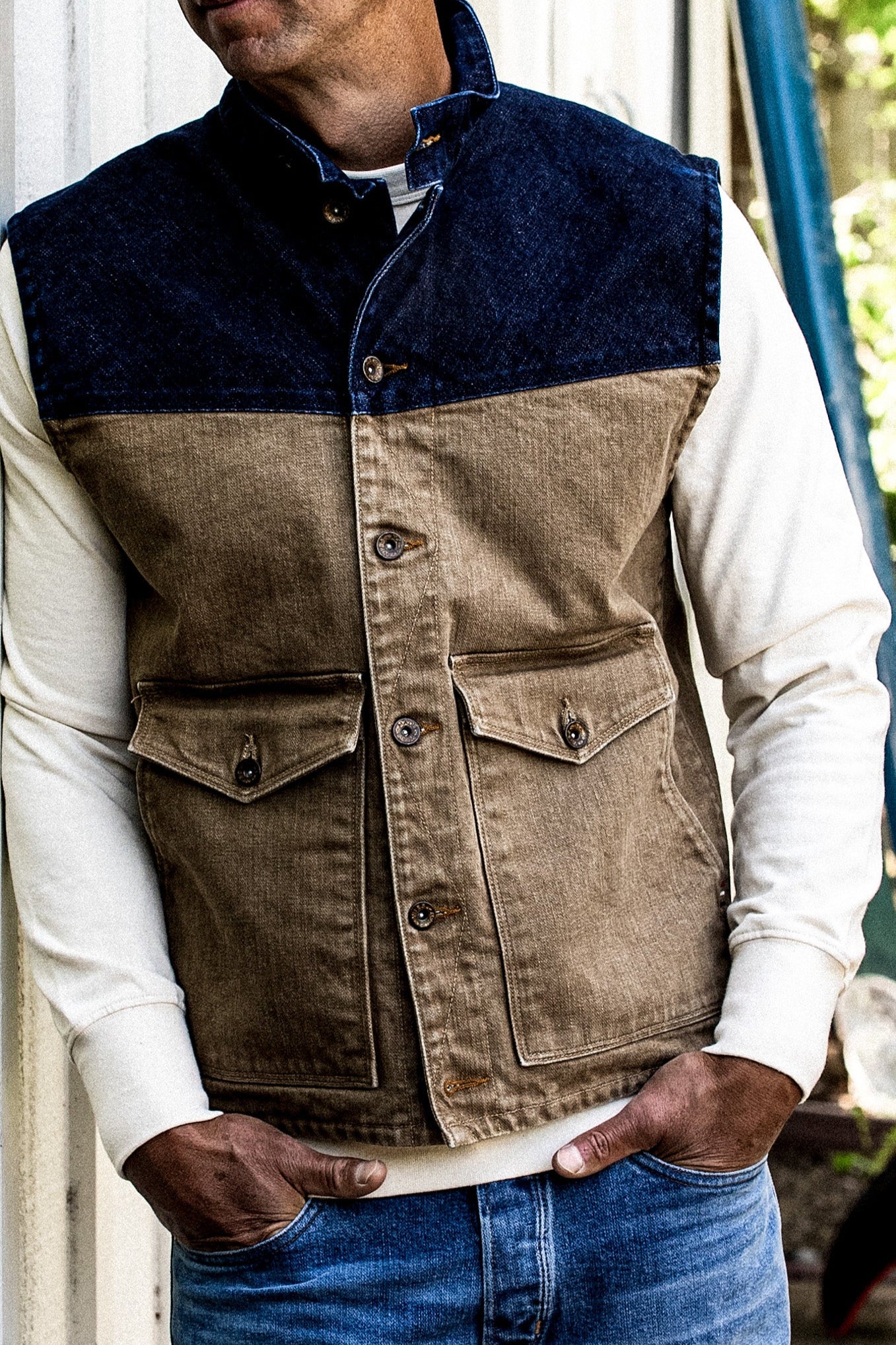 Man wearing a two-tone broken twill denim vest with indigo yoke and wheat body over a cream long-sleeve shirt.