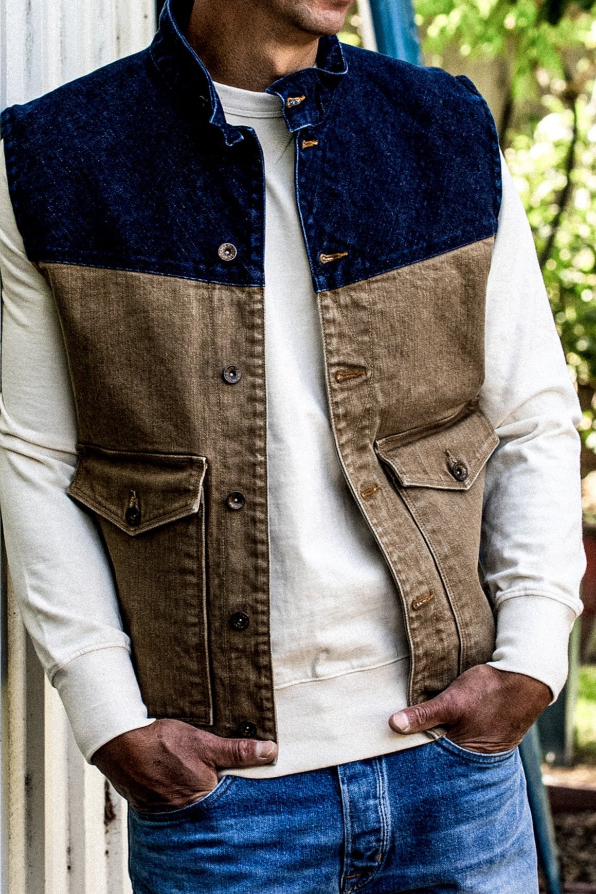 Man wearing a two-tone broken twill denim vest with indigo yoke and wheat body over a cream sweatshirt.