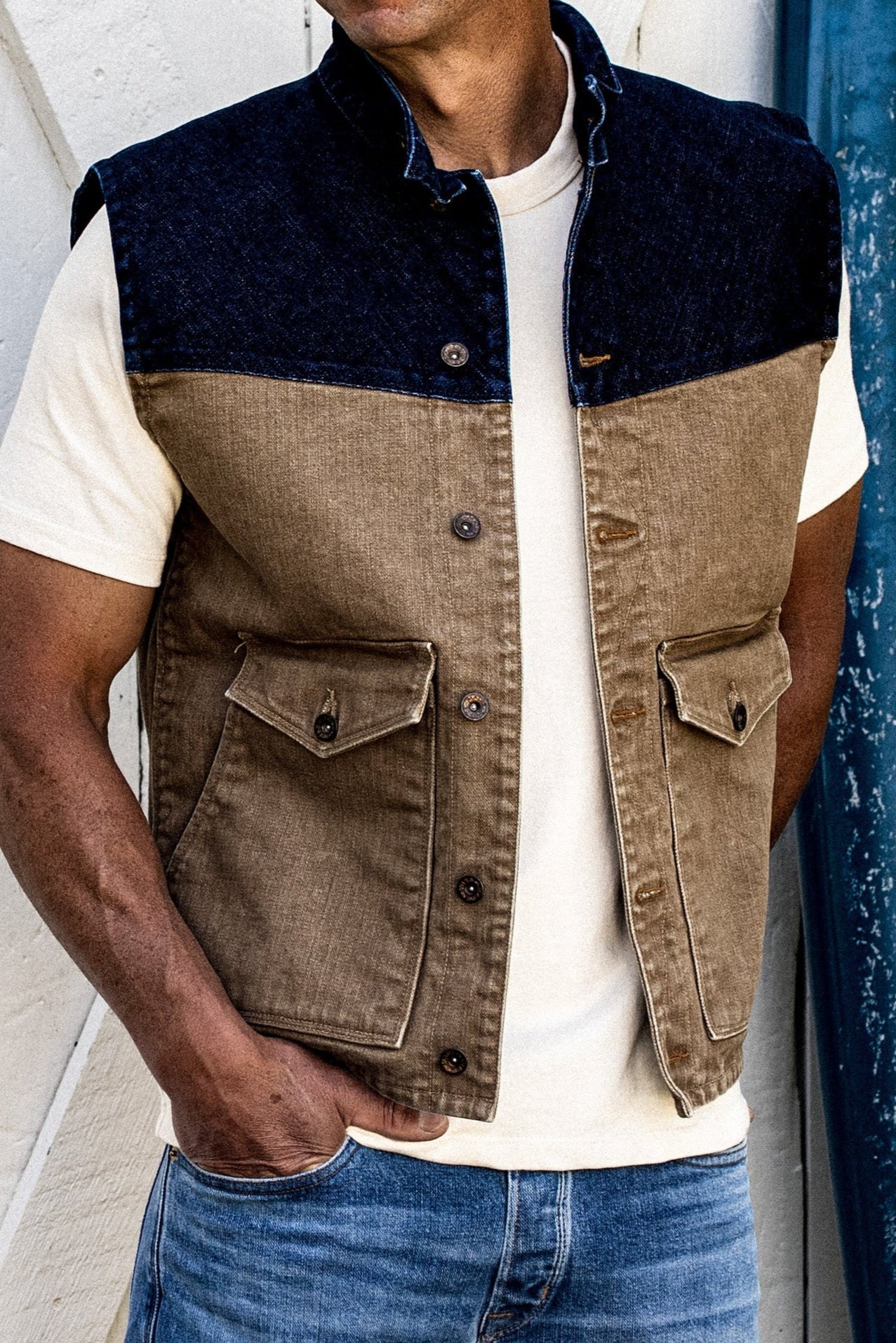 Two-tone broken twill denim vest with indigo yoke and wheat body, worn over a cream tee.