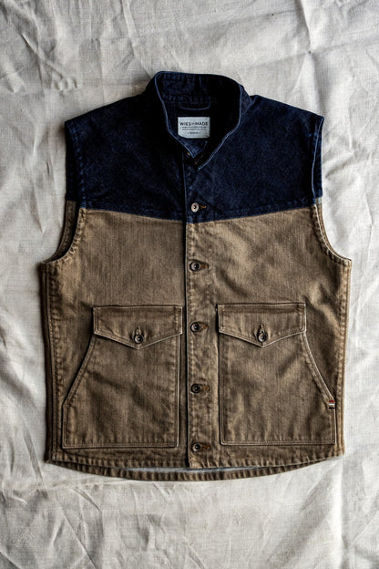 Wheat broken twill denim vest with indigo yoke, brass buttons, and double chest pockets laid flat on linen.