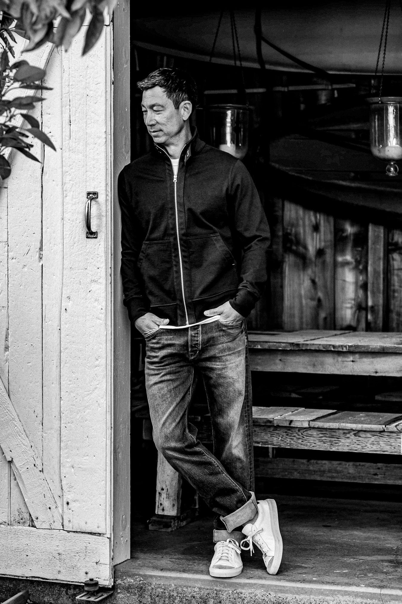 Man leaning in a wooden doorway wearing a full-zip men's cotton moto jacket.