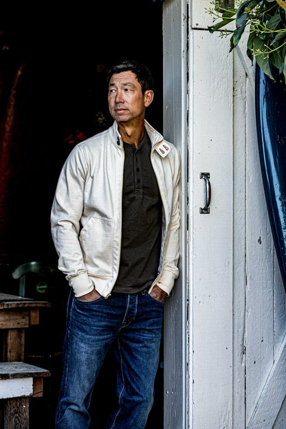 Man wearing an open natural cotton Stinson moto zip jacket over a dark henley and jeans.