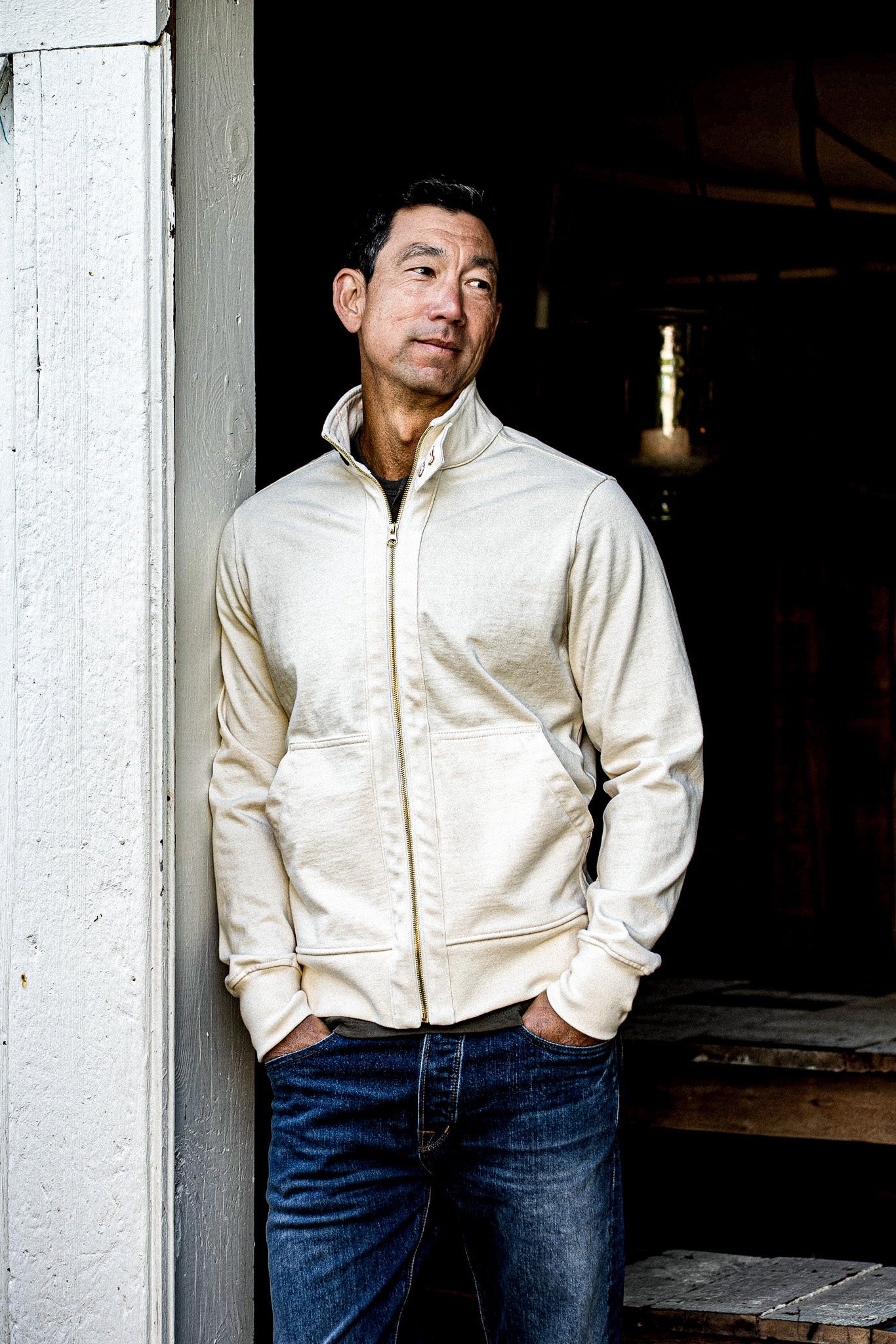 Man wearing natural Stinson Moto zip jacket in 12oz cotton, leaning against a doorway.
